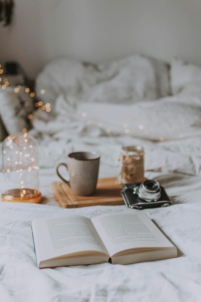 Image of open book on a bed with mug and camera.