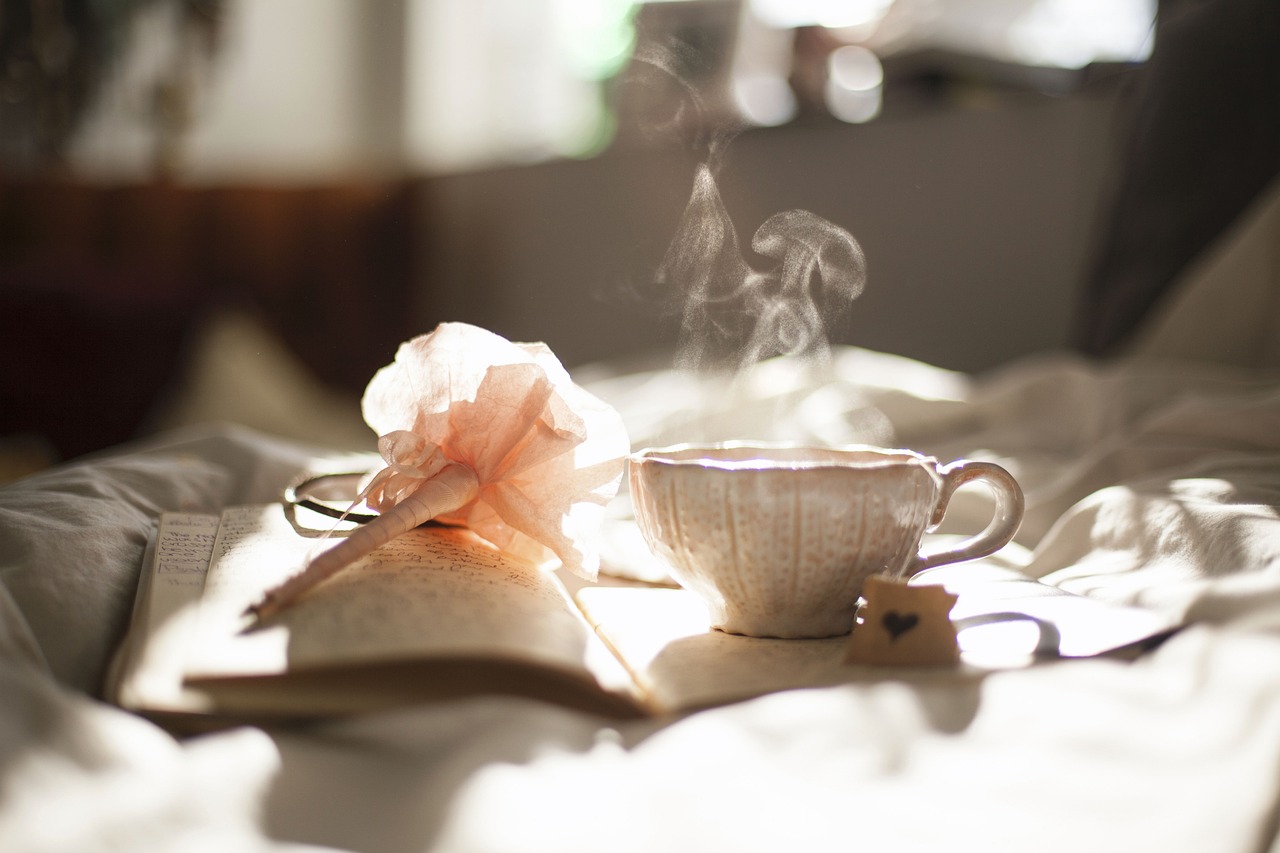 Image of mug and a book with a flower pen on a bed.