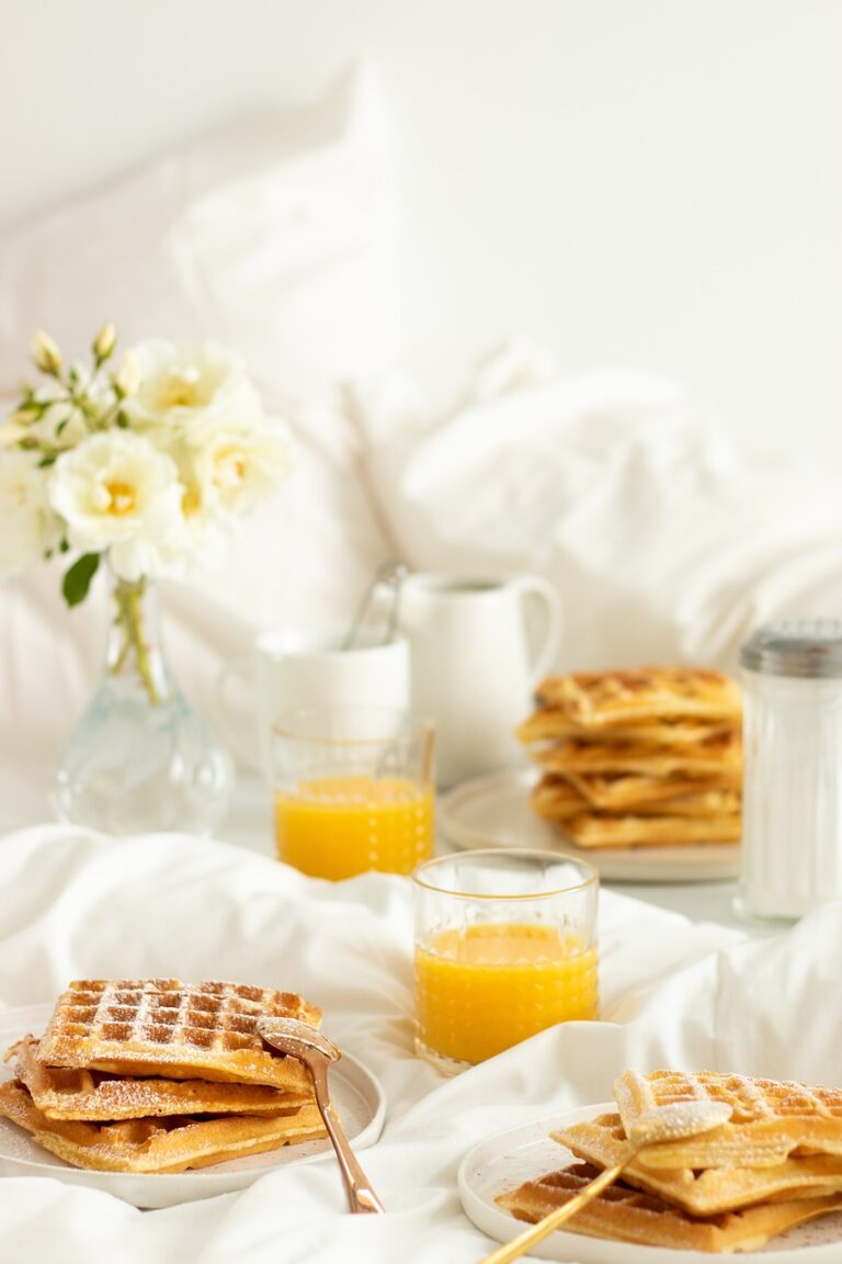 Image of breakfast on bed with waffles, juice, and flowers.