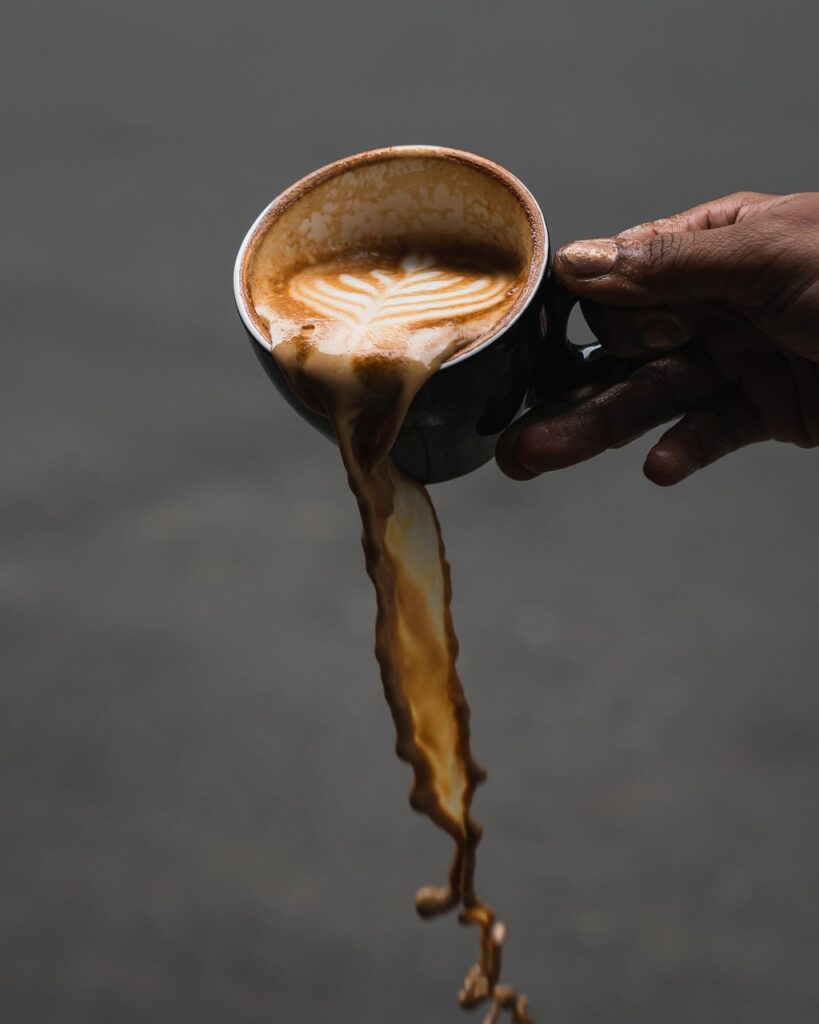 Image of a hand tilting over a mug of coffee. 