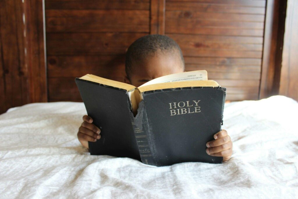 Image of a child in bed reading his bible.