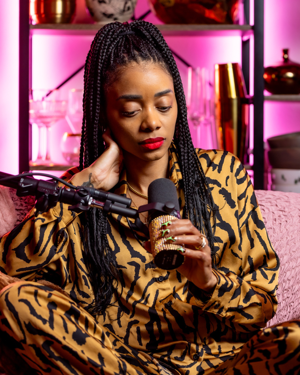 Shanika sitting on the couch with the microphone in animal print outfit. 