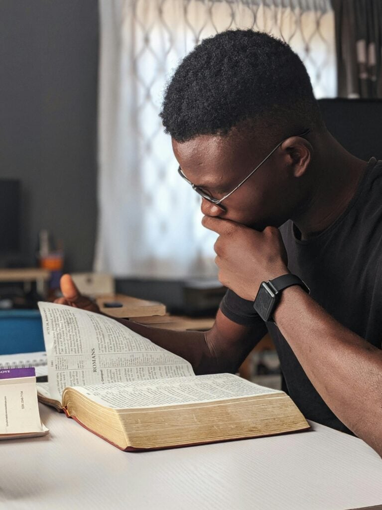 A guy reading the bible on a table in contemplation.