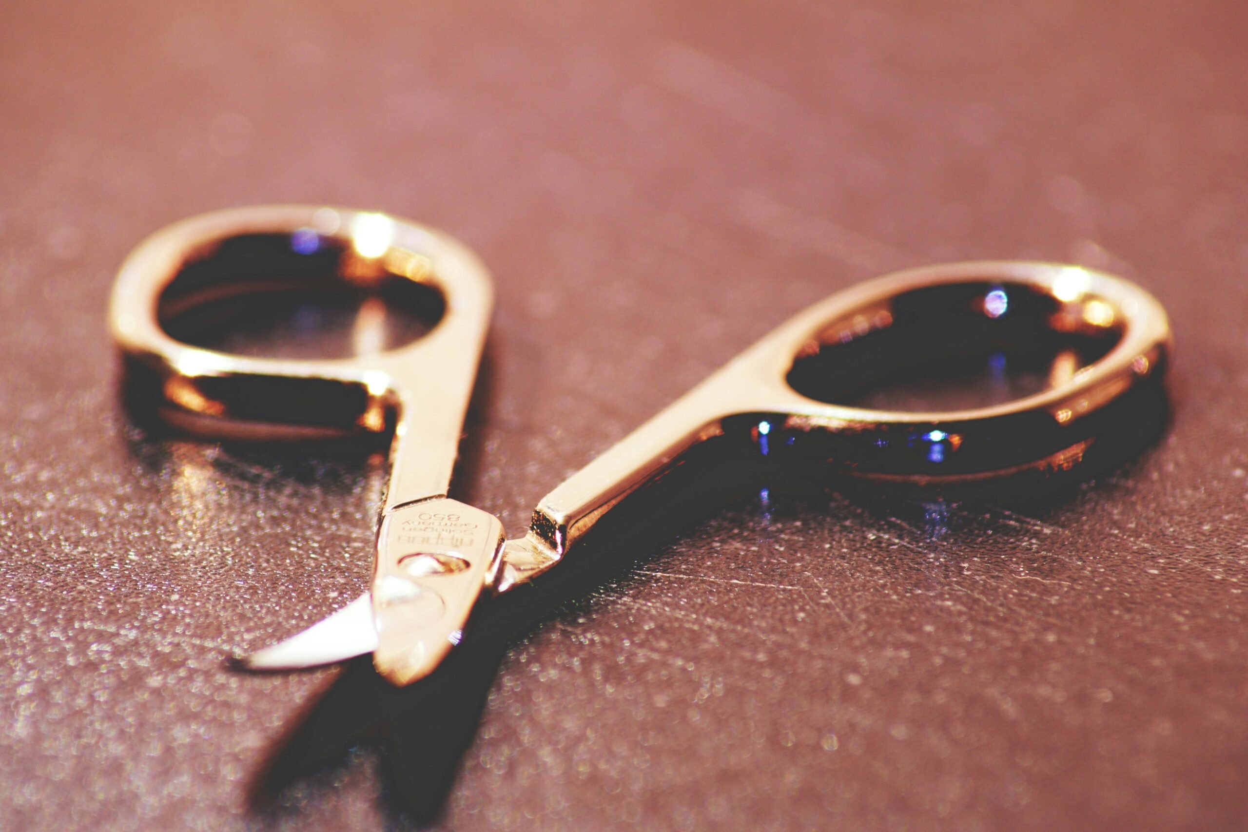 Up close shot of a pair of gold scissors laying on a surface.