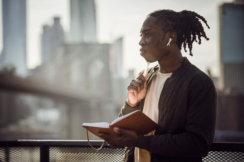Image of a man looking forward and holding a journal and pen in reflection.