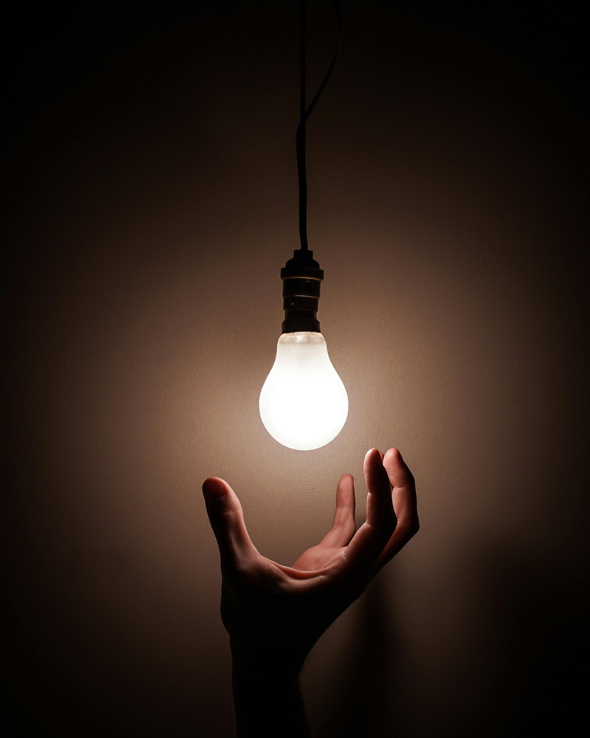 A hand reaching to hold a light bulb in a dark room.