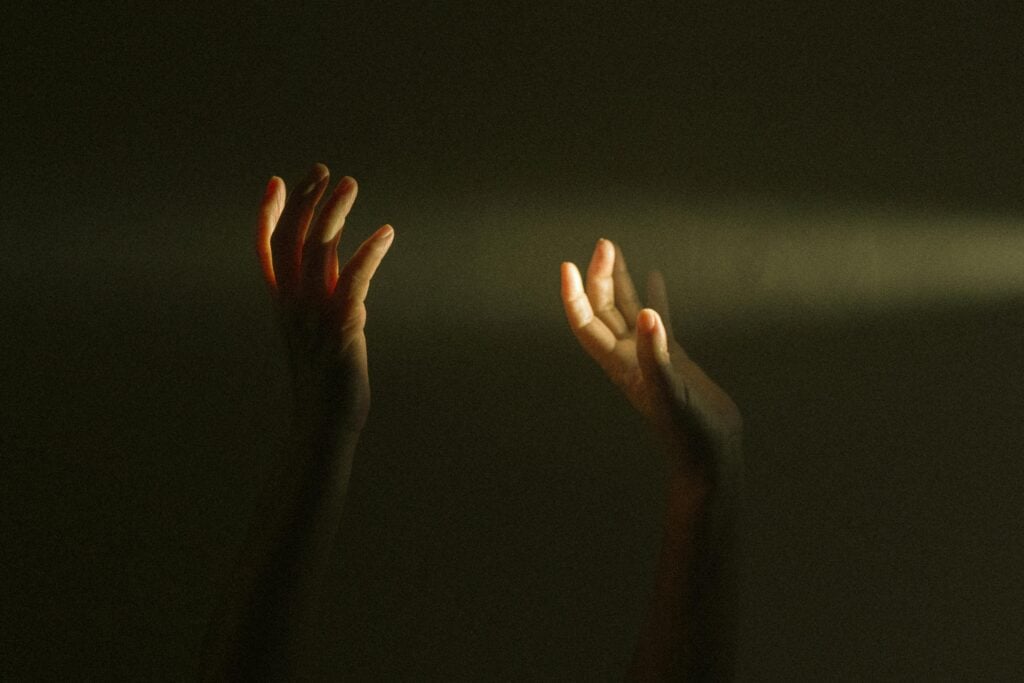 Hands raised in between dark and light.