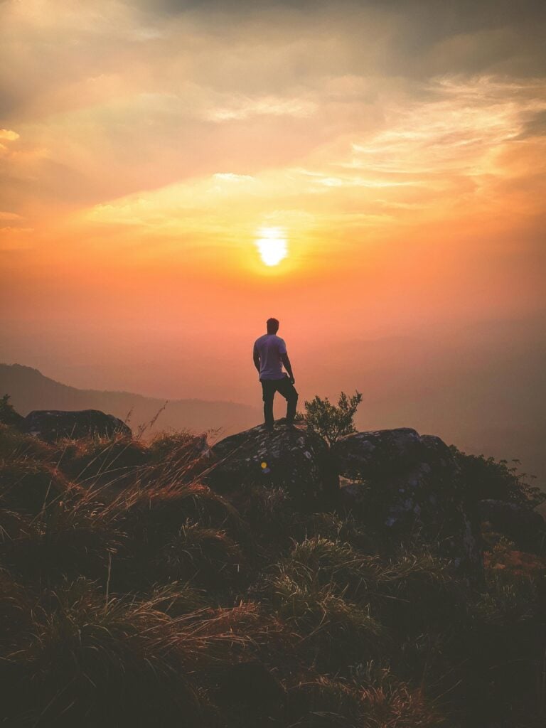 A person standing on a hill looking at the sunset.