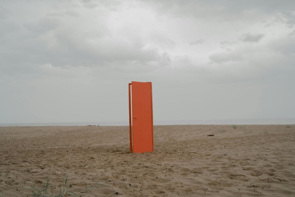 An image of an orange door halfway opened on a desert.
