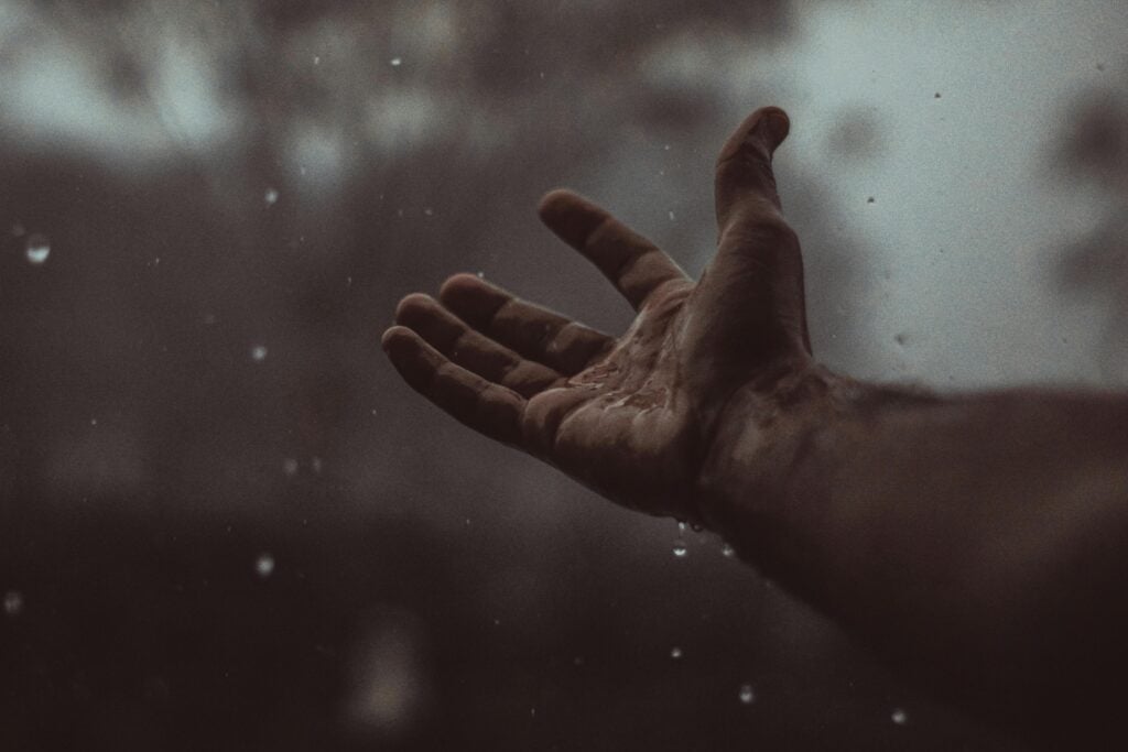 Man hands reaching out in gloom and rain.