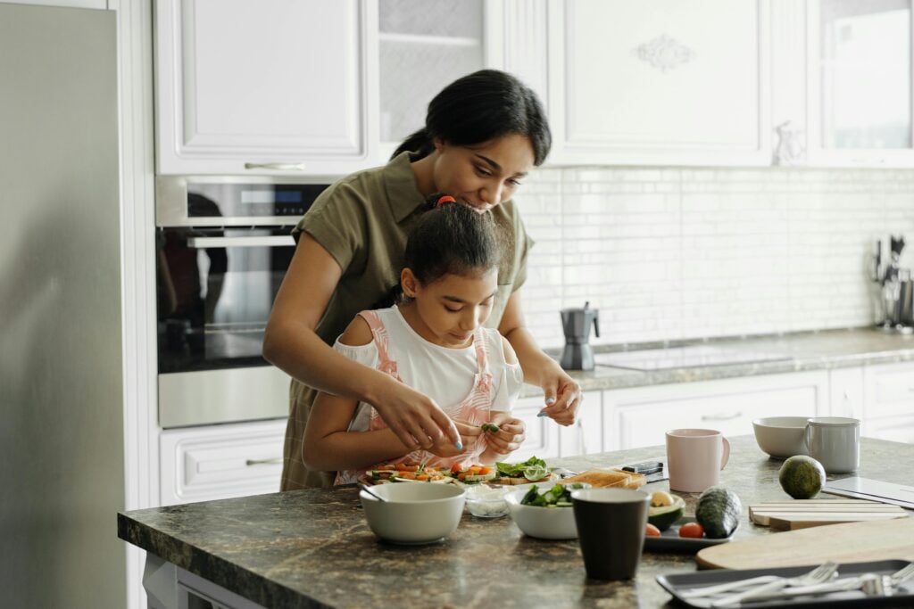 A mother and daughter standing together and preparing food in the kitchen.