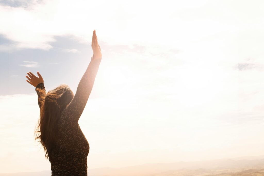 Image of someone outdoors lifting their hands to the sky.