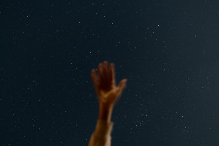 A hand risen upward in the sky full of stars.