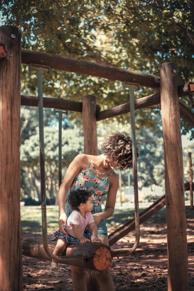 A mother and child on a swing on the playground.