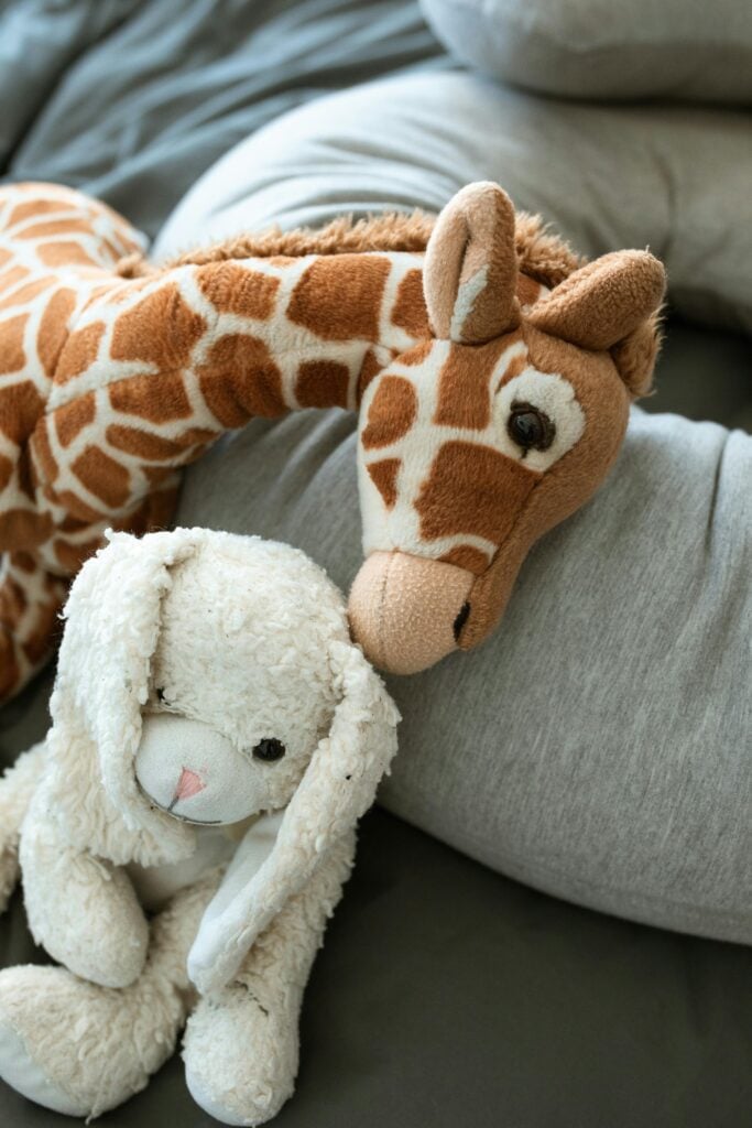 Stuffed animals and a grey pillow on a bed.