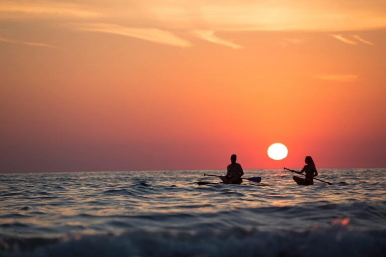 Image of two people canoeing on water in the sunset.