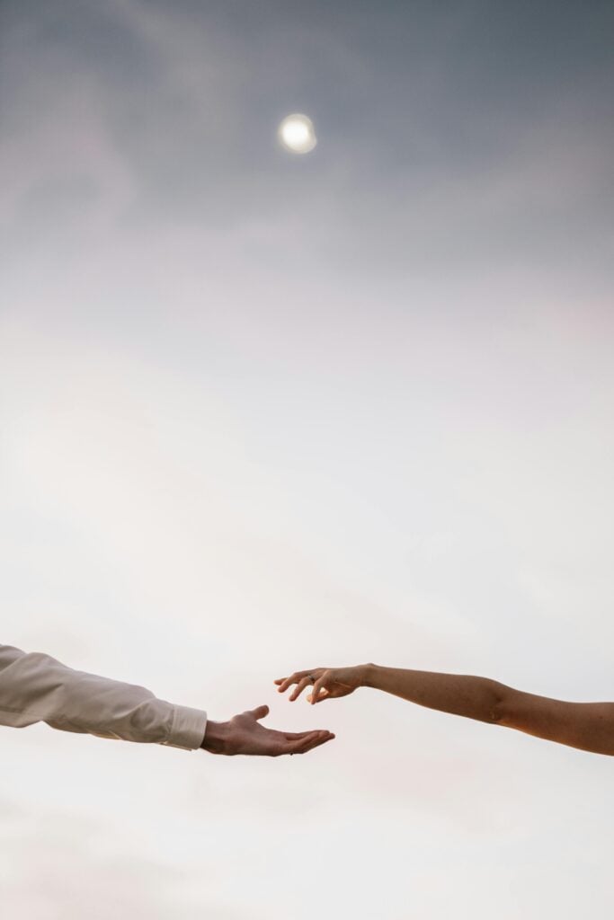 Two hands towards each other with a view of the sky.