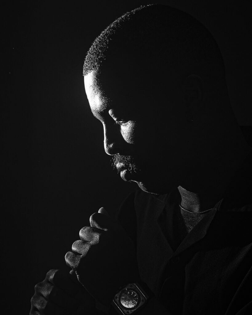 A guy looking down in a dark black background.