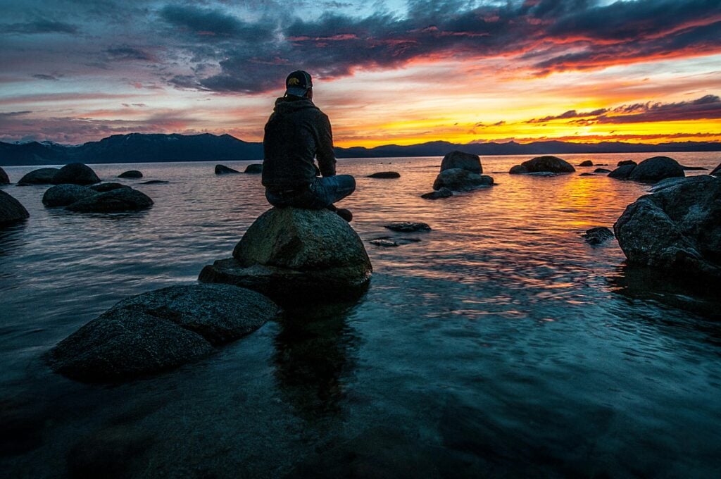 A guy sitting on a rock in the middle of the ocean.