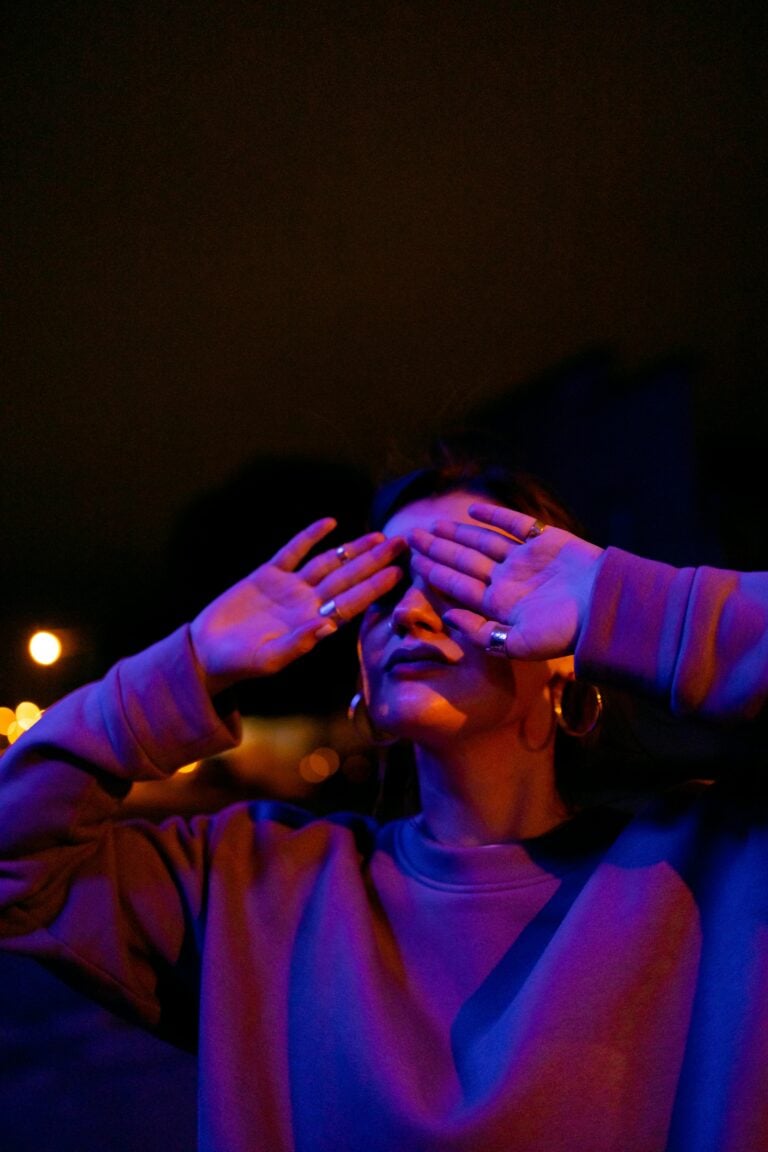 A woman in a purple background with hands covering face.