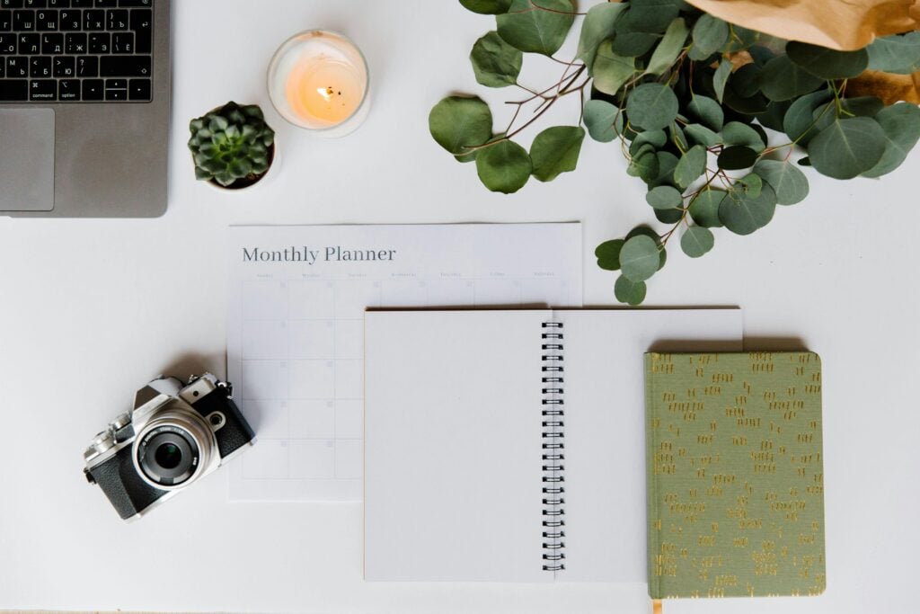 Journal, planner, camera, and laptop on a white desk.