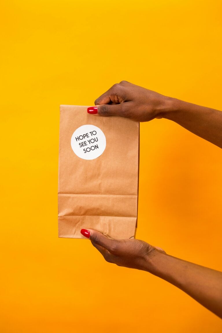 Woman hands holding up a paper bag with a yellow-orange background.