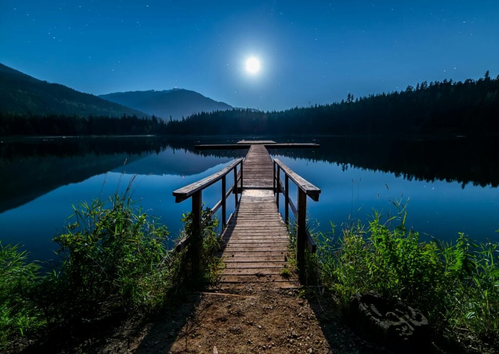 A crosswalk in front of a lake with the moon shining in the sky.