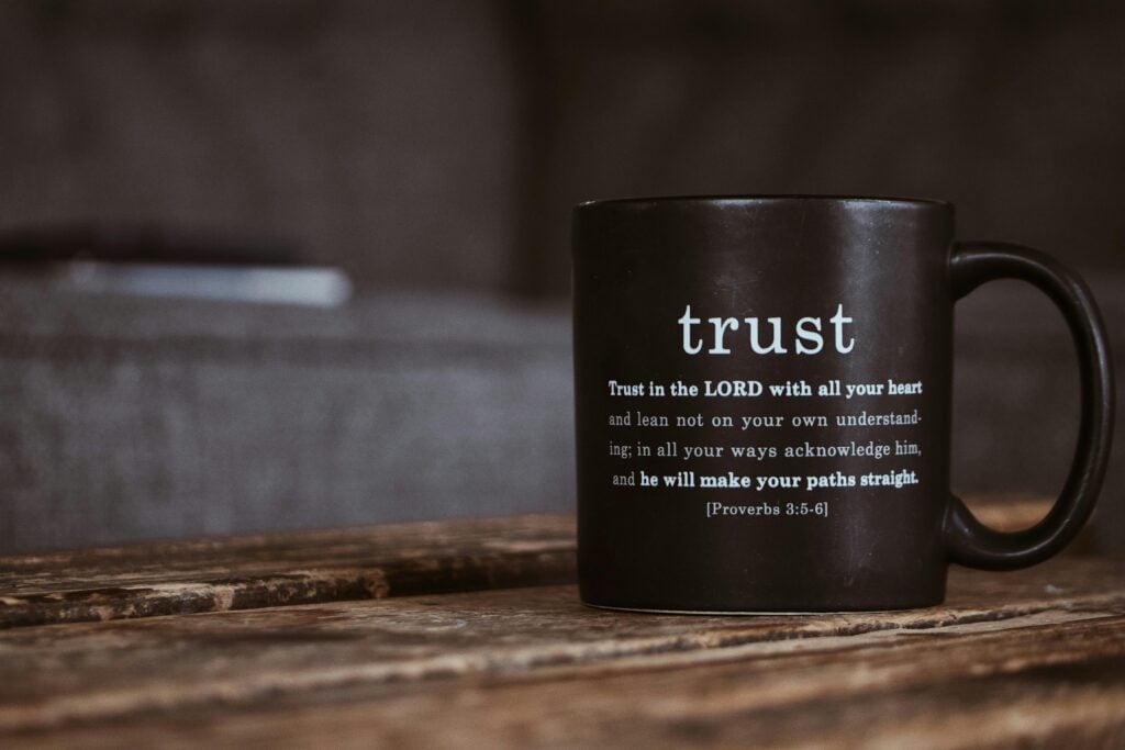 A black mug with scripture sitting on a wood table.