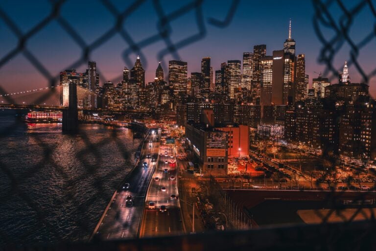 View through a broken fence of a city at night.
