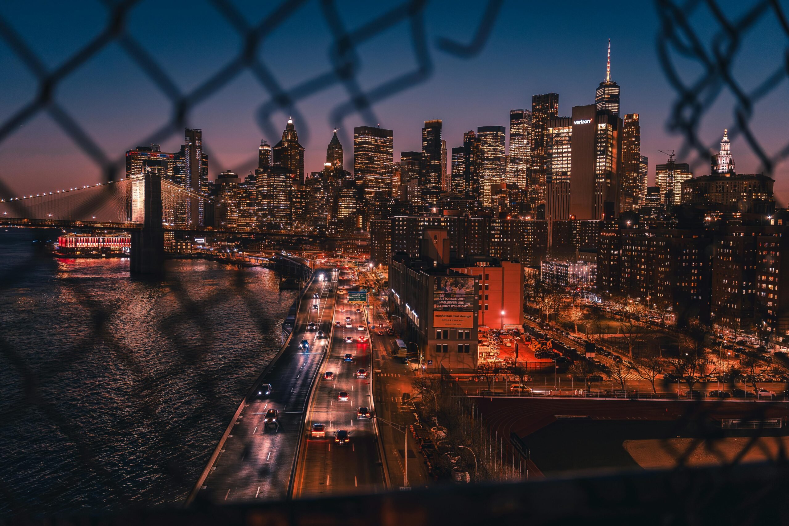 View through a broken fence of a city at night.