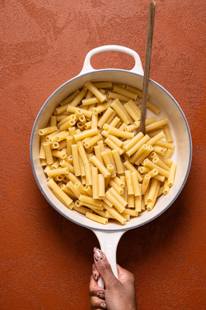 Cooked pasta in a pot with a wooden spoon held by a woman hand.