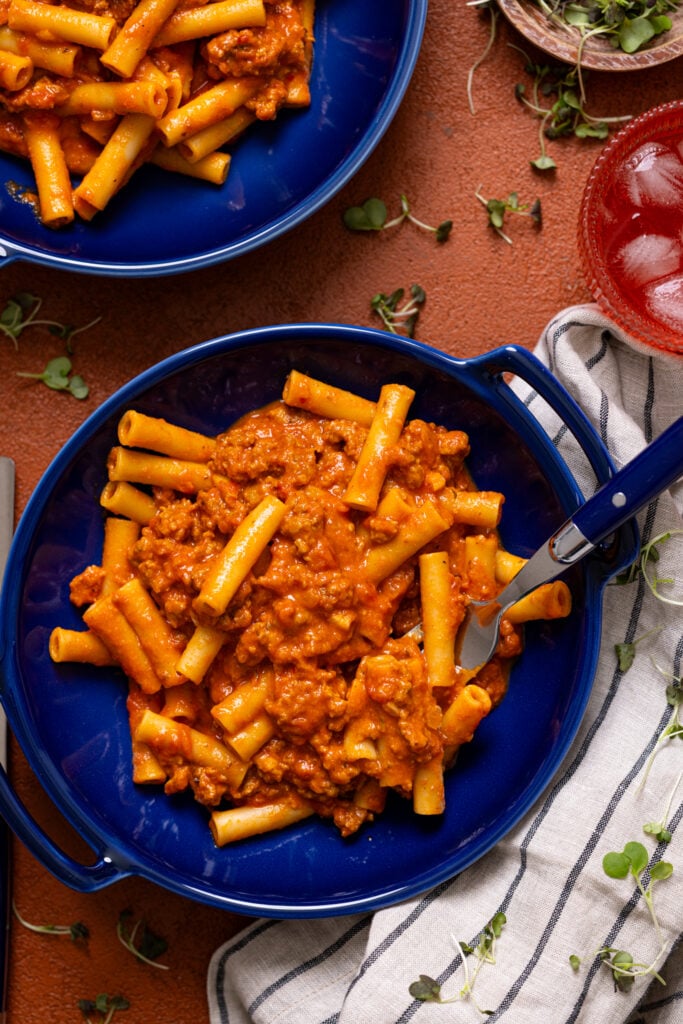 My Childhood Homemade Beefaroni in two bowls with a fork and a drink.