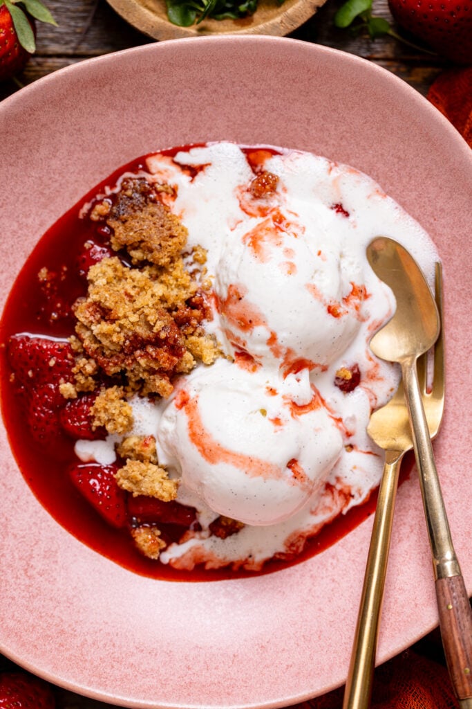 Up close shot of Strawberry Crumble For Two in a pink bowl with utensils.