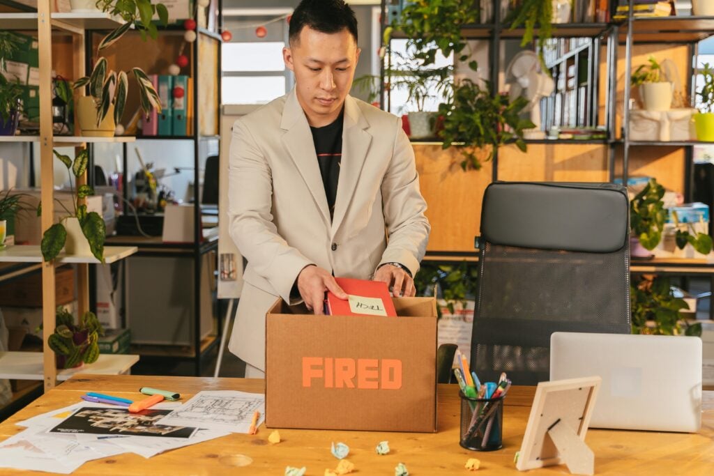 A guy packing a box at his office desk that says fired.