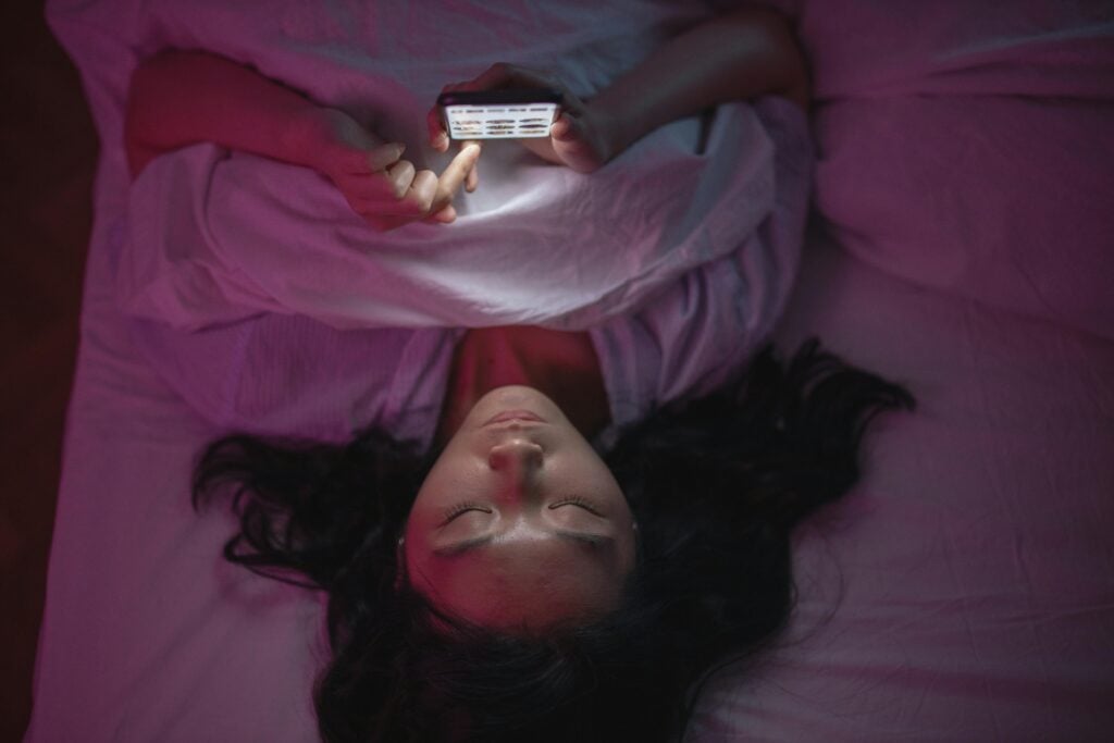 A woman laying on bed while scrolling on her phone.
