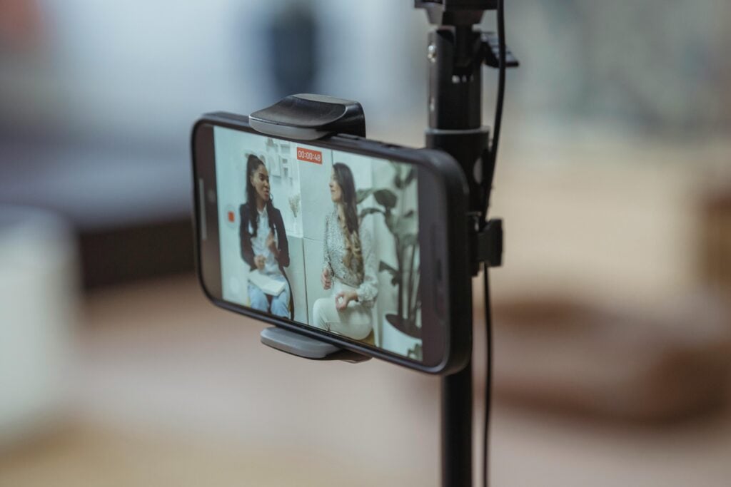 Two women showing on the screen of a phone on a tripod.
