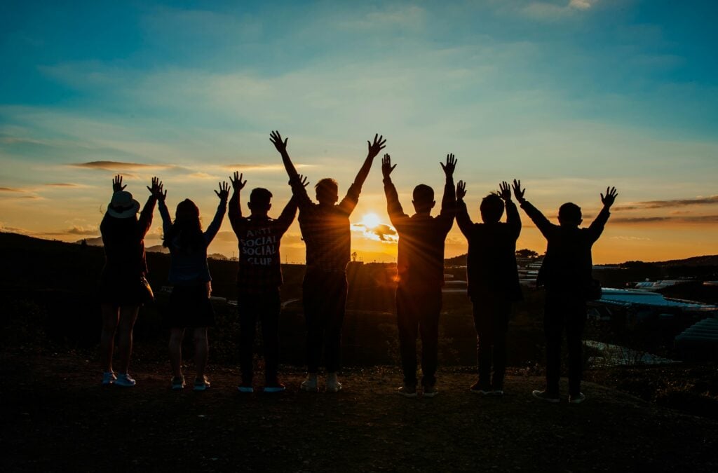 A group of young people looking at the horizon with hands lifted.