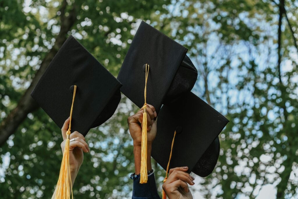 Hands in the air with graduation caps in their hands.
