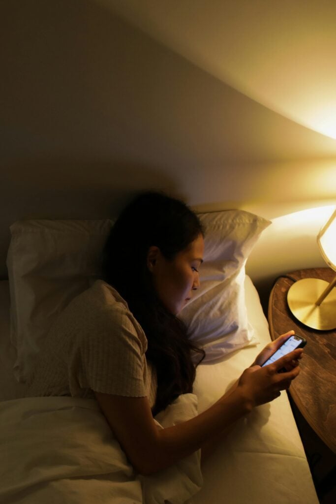 A woman lying in bed looking at her phone.