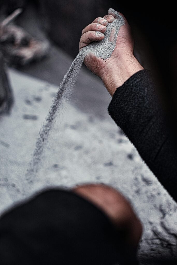 A person holding grey sand in their hand and letting it fall.