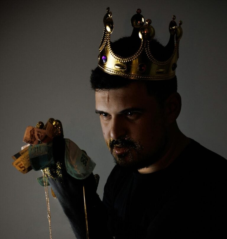 A man with a gold crown and glitter holding bank notes or money with a slight sinister look.
