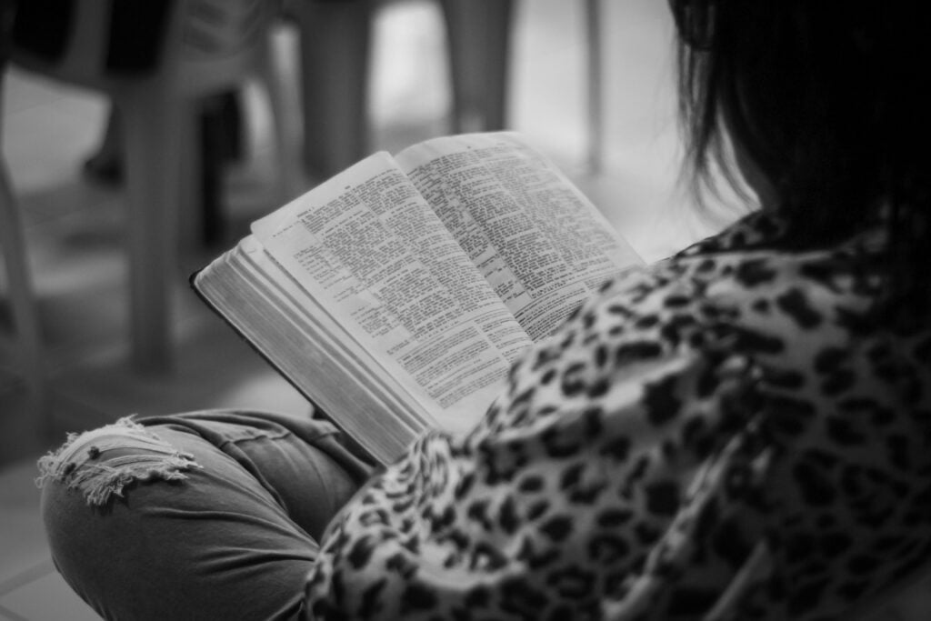A woman in a leopard sweater sitting reading the text or bible.