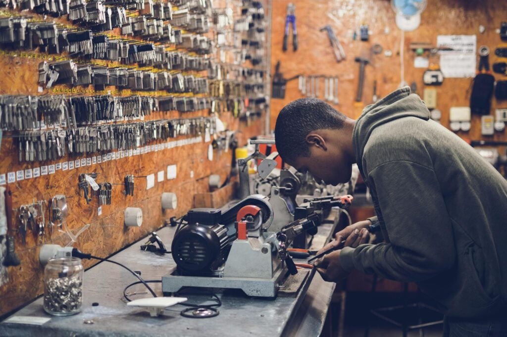 A guy focused and working hard on keys using a machine in a garage.
