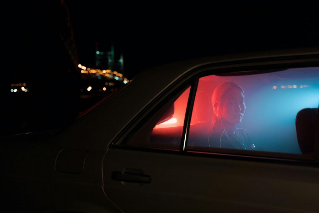 Someone in a car in the night time with blue/red light illuminating.