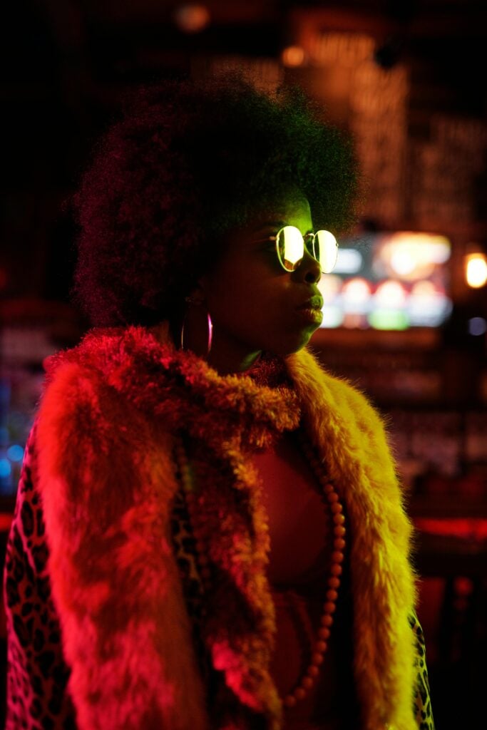 A female with a fur scarf looking ahead with shade in a dark background outside.