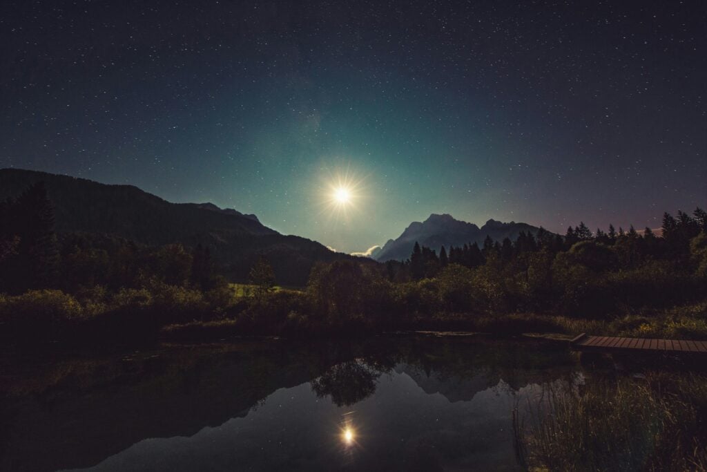 A nighttime view of mountains by water with a bright moon or star.