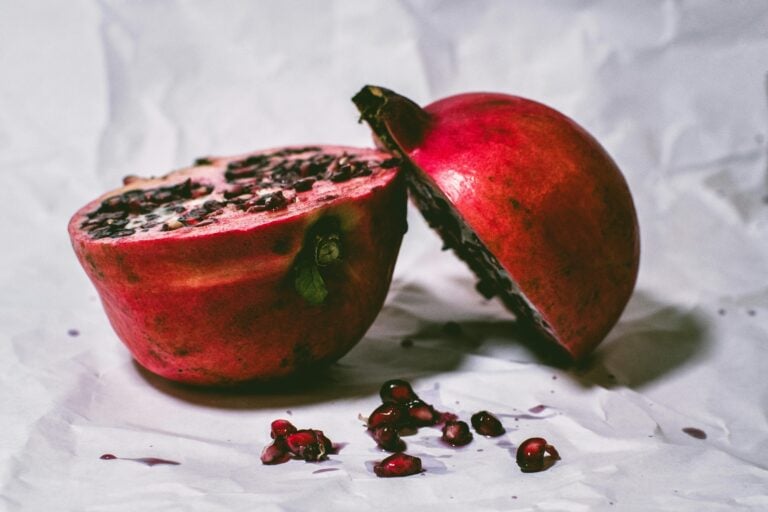 A pomegranate sliced in half on a white surface with seeds.