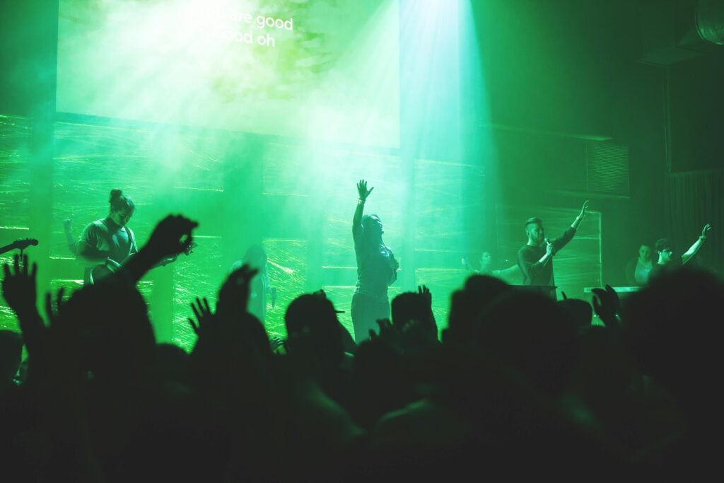 A group of worshipers in a church sanctuary with green lights and stages.