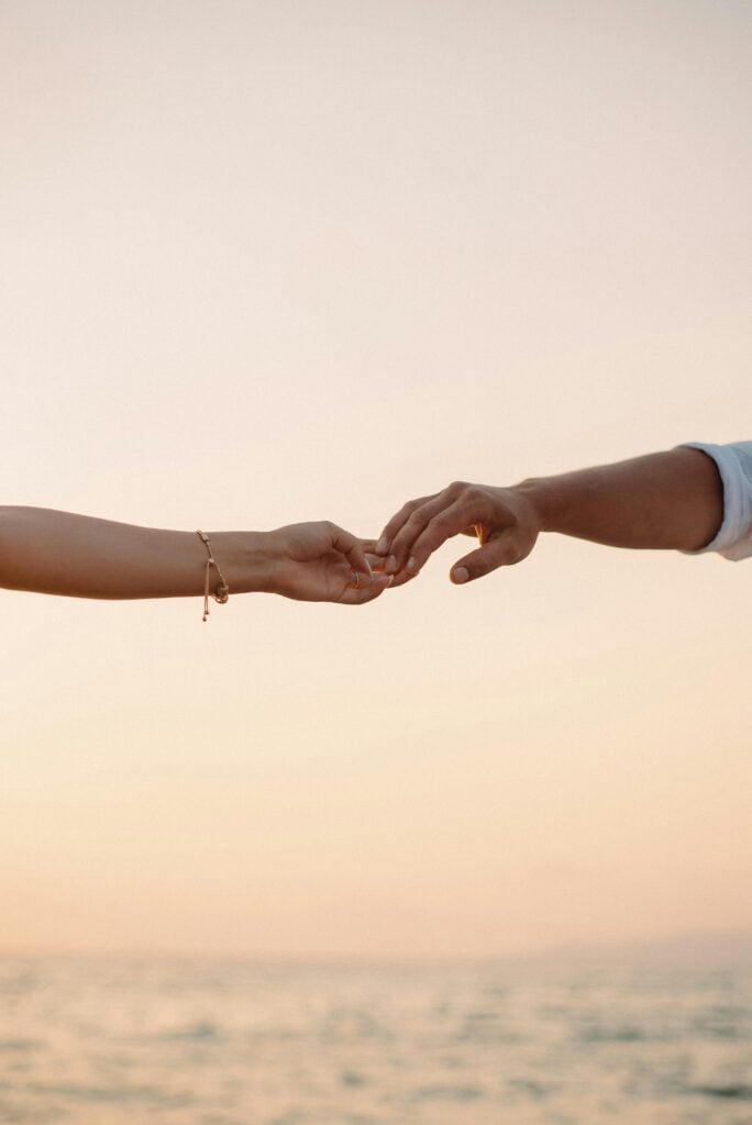 Two hands holding each other in front of an ocean view.