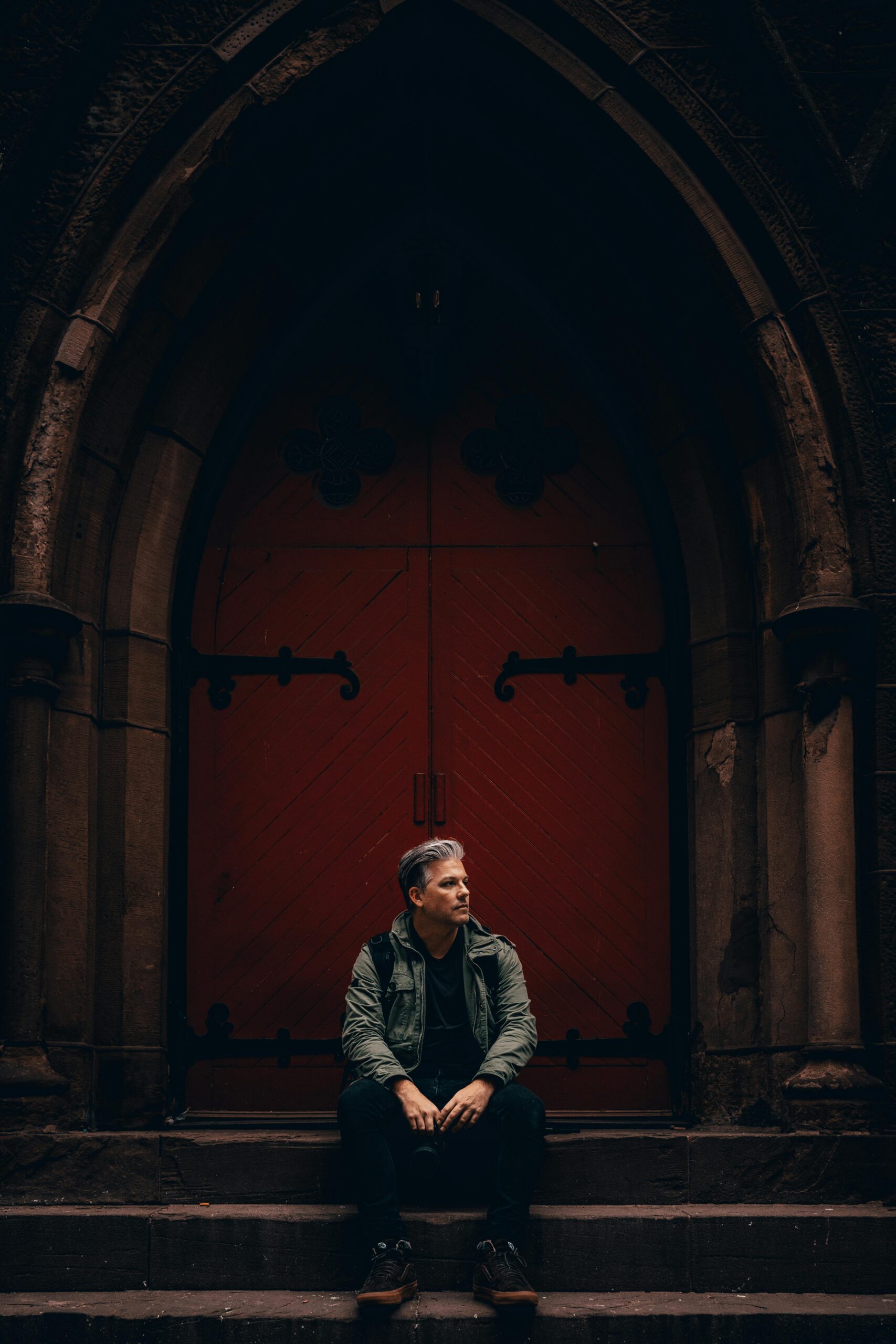 A man sitting outside a church with red doors.